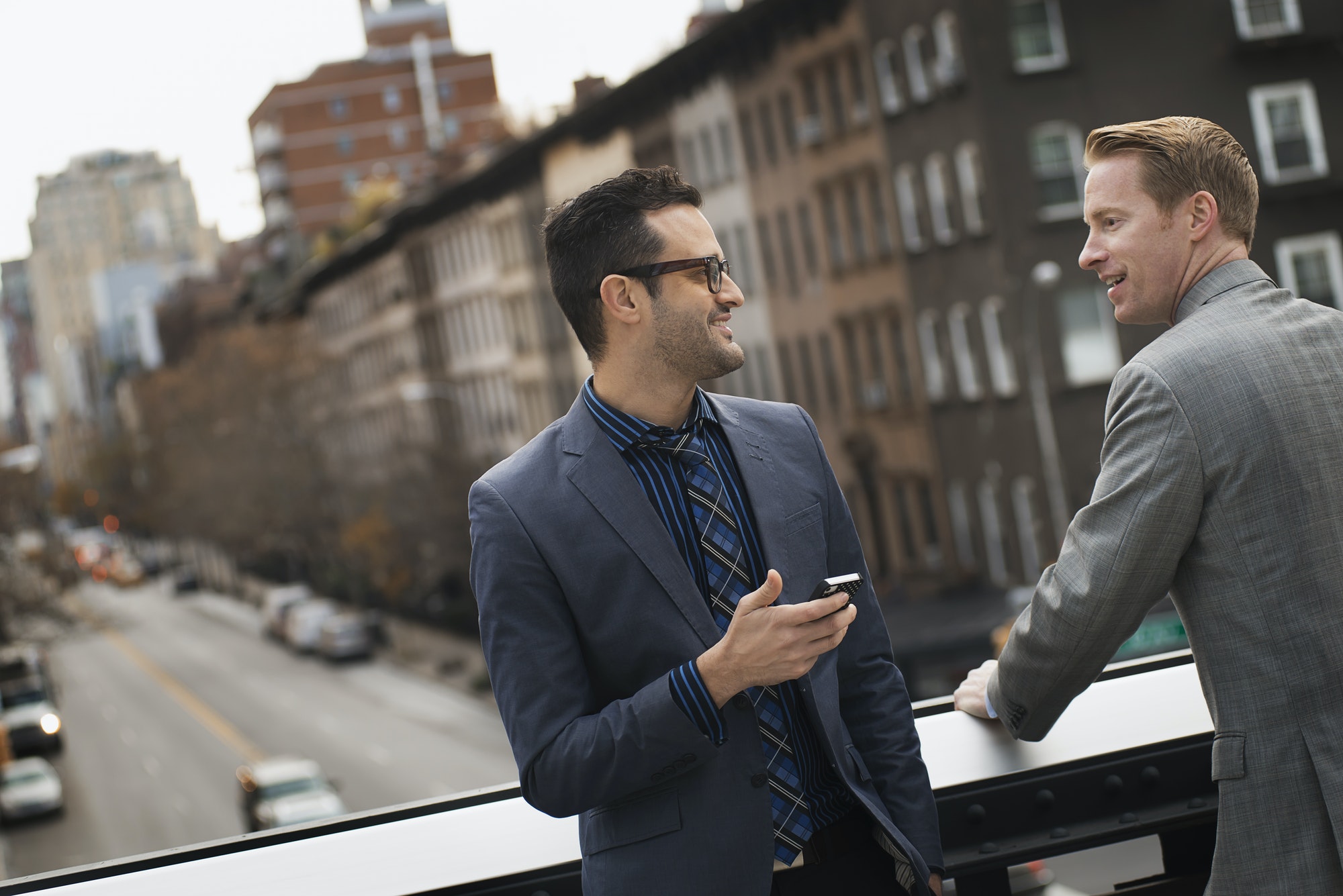 Two men standing talking on an elevated walkway above a city road.